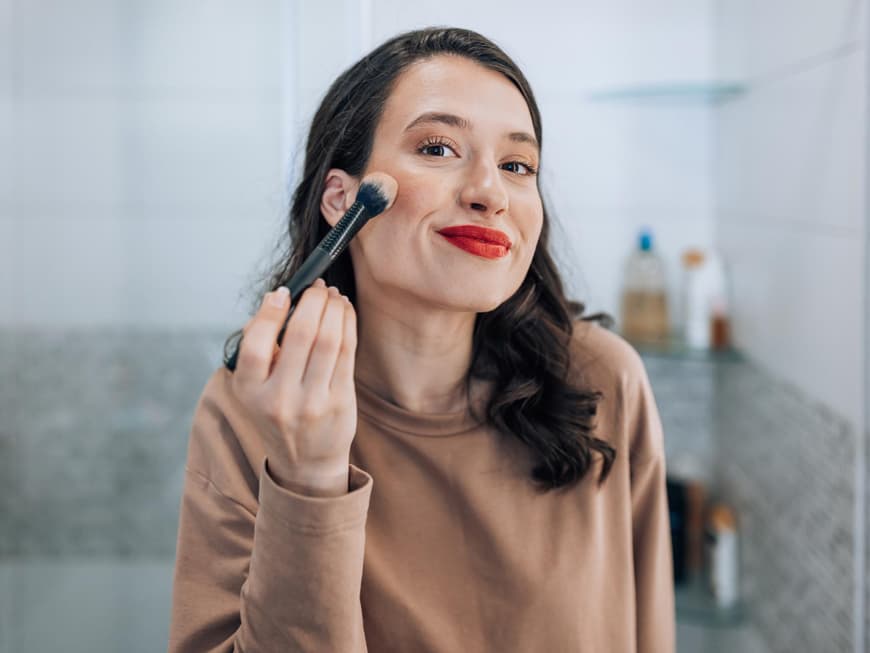 Candy Cane Blush ist der neue Trend für Weihnachten. Frau trägt sich Rouge auf die Wangen auf und hat rote Lippen geschminkt.