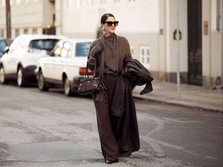 Frau trägt ein komplett braunes Outfit mit Hose, Pullover und Tasche und einer Sonnenbrille.