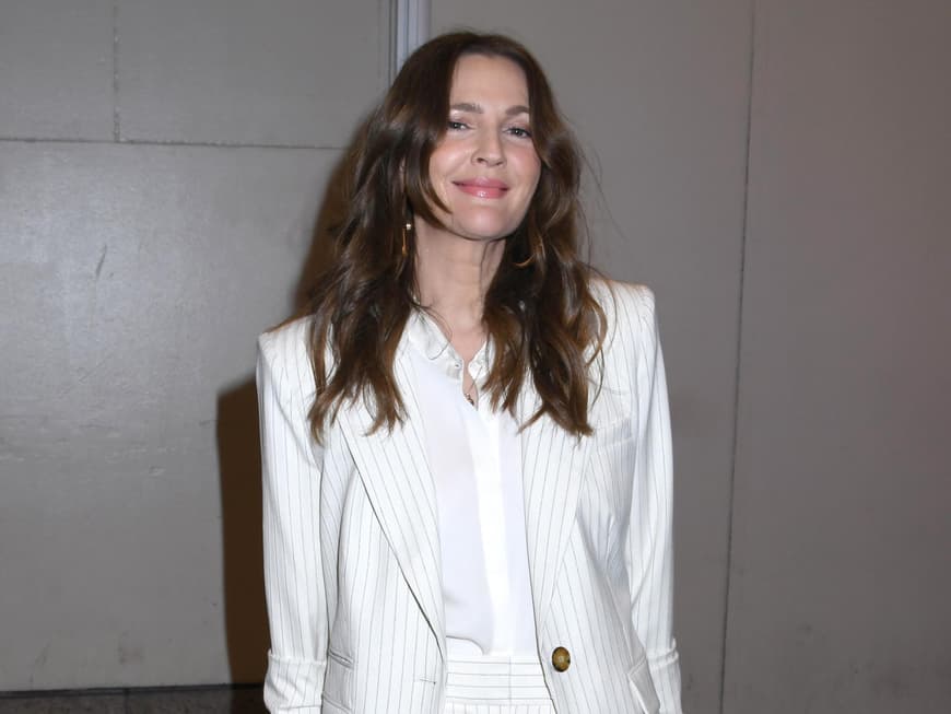 Drew Barrymore mit offenen Haaren und einem weißen, gestreiften Anzug.
