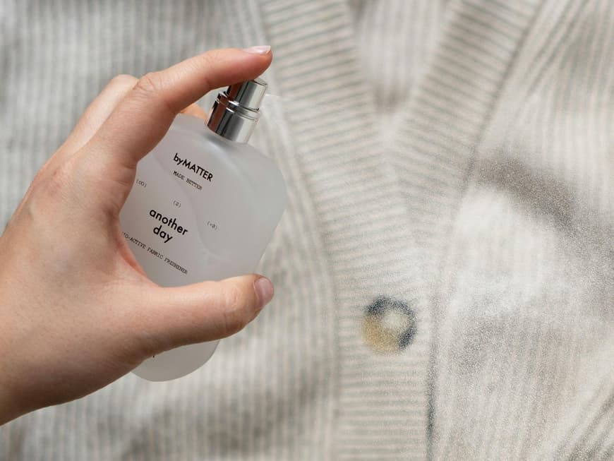 Jemand sprüht ein Parfum auf eine Strickjacke.