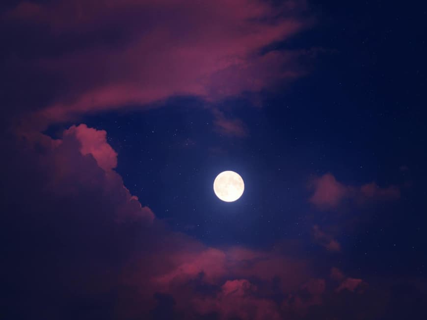 Ein Vollmond an einem blauen Himmel mit rosafarbenen Wolken.