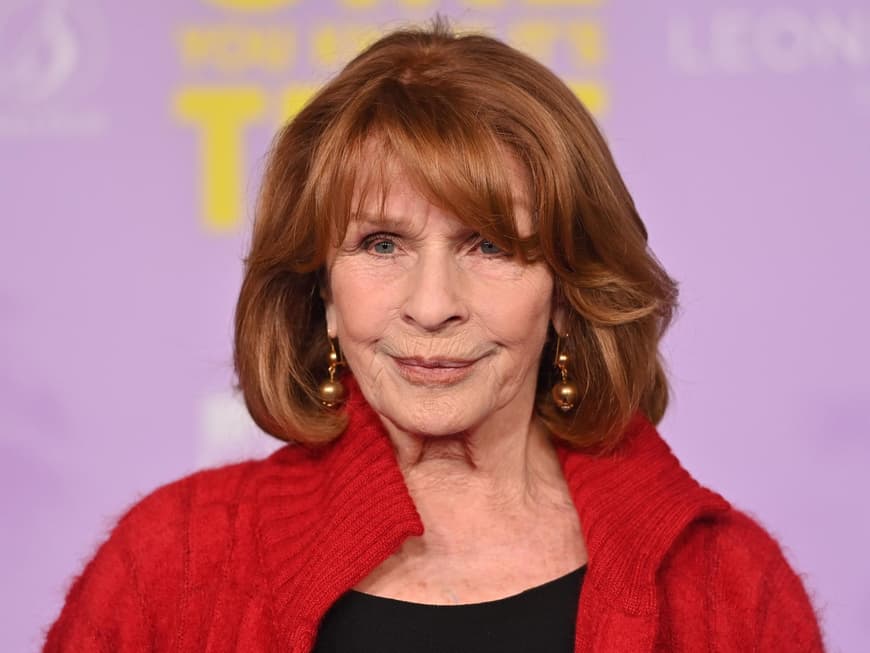 Senta Berger war fast 60 Jahre verheiratet. Senta Berger mit goldenen Ohrringen und einer roten Strickjacke.