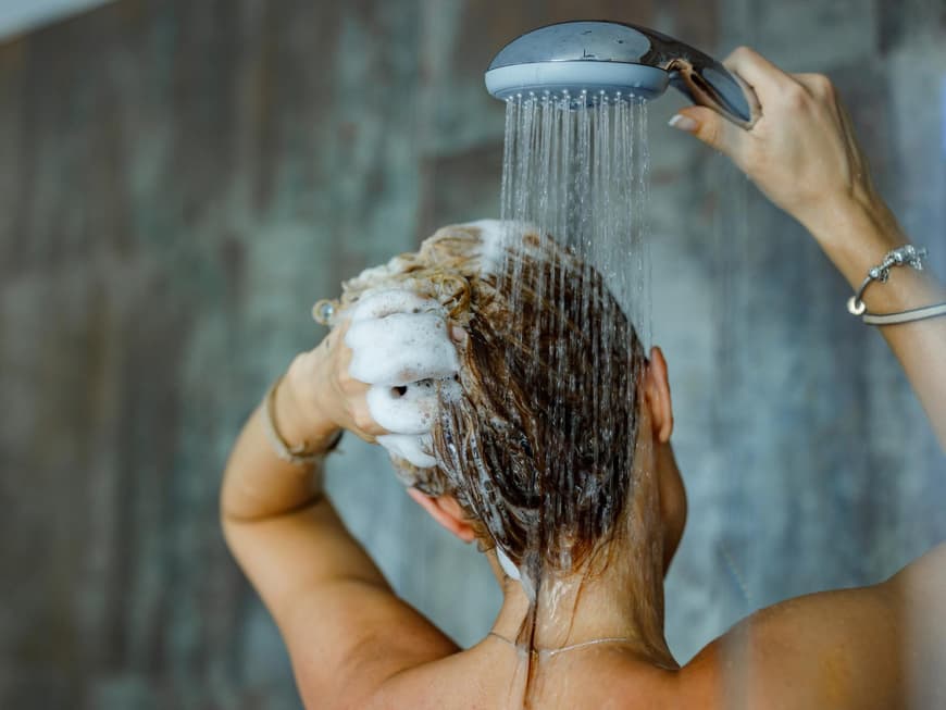 Frau wäscht sich in der Dusche die Haare und braust sie mit Wasser ab.