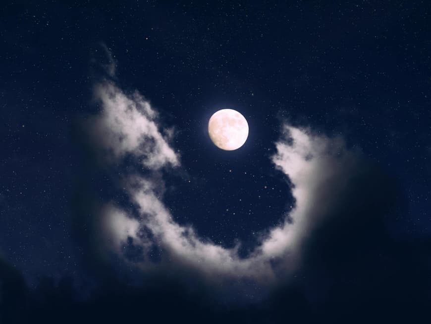 Ein Vollmond findet etwa einmal im Monat statt. Vollmond guckt am Sternenhimmel zwischen Wolken hervor.