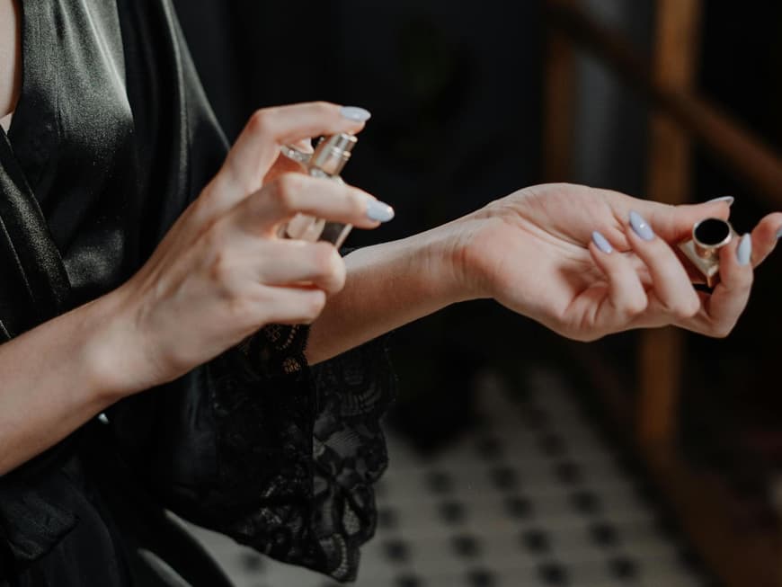 Frau sprüht sich ein Parfum auf das Handgelenk und trägt ein schwarzes Nachthemd.
