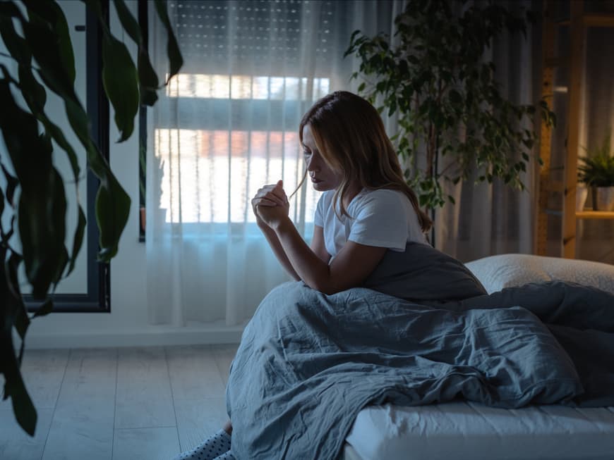 Frau sitzt traurig und allein im Bett