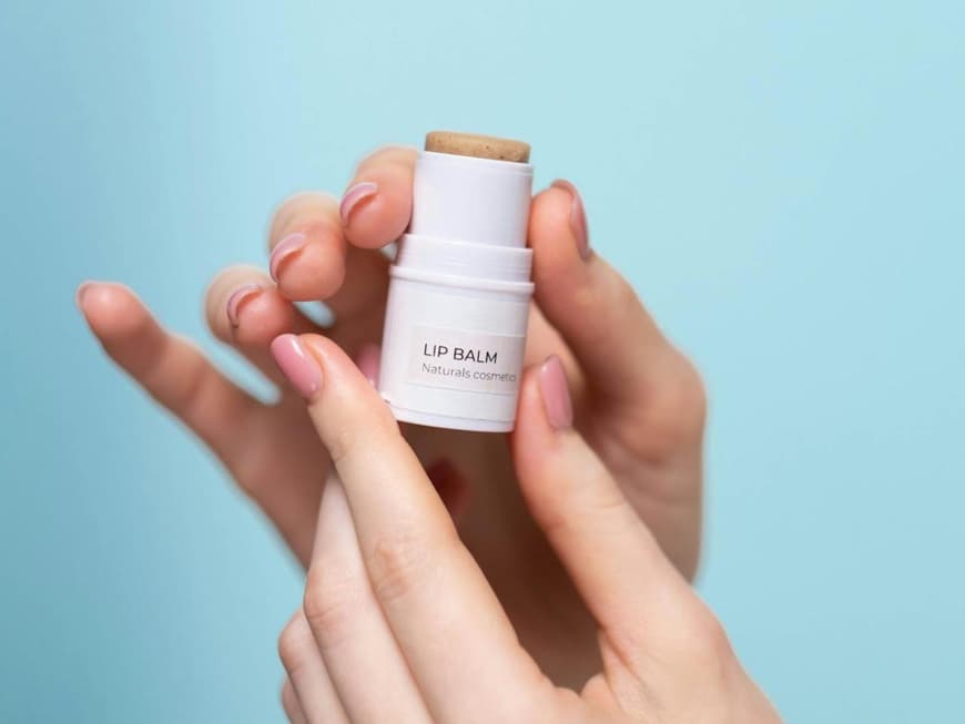 Ein Lip Balm wird in der Hand vor einem hellblauen Hintergrund gehalten.