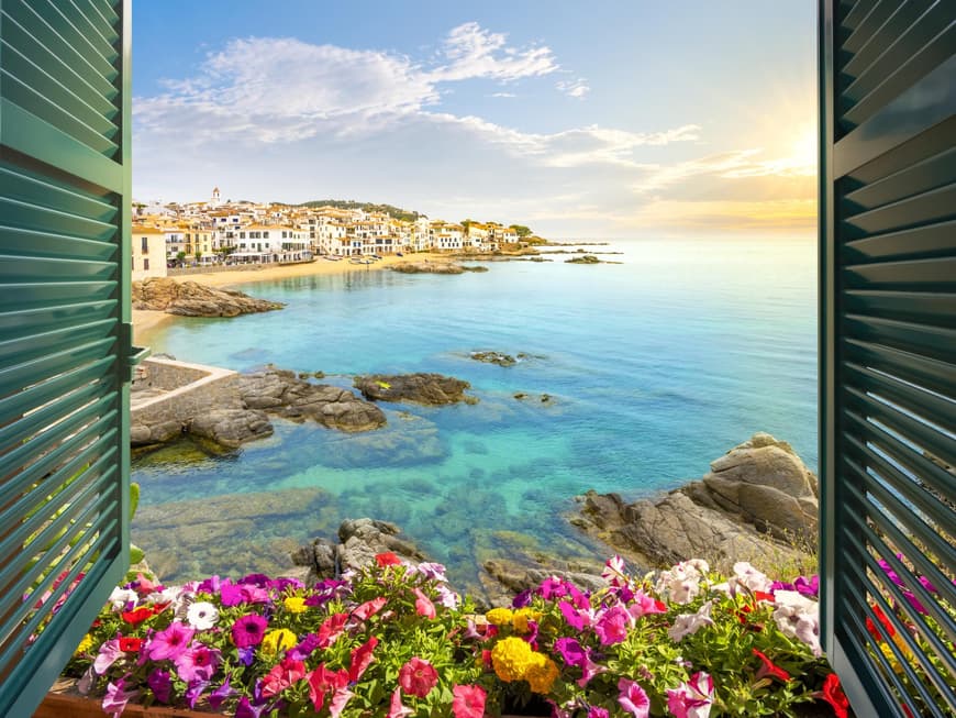 Die Costa Brava überzeugt mit türkisfarbenem Wasser. Blick aus einem Fenster der Costa Brava auf das Meer mit Häusern an der Küste.