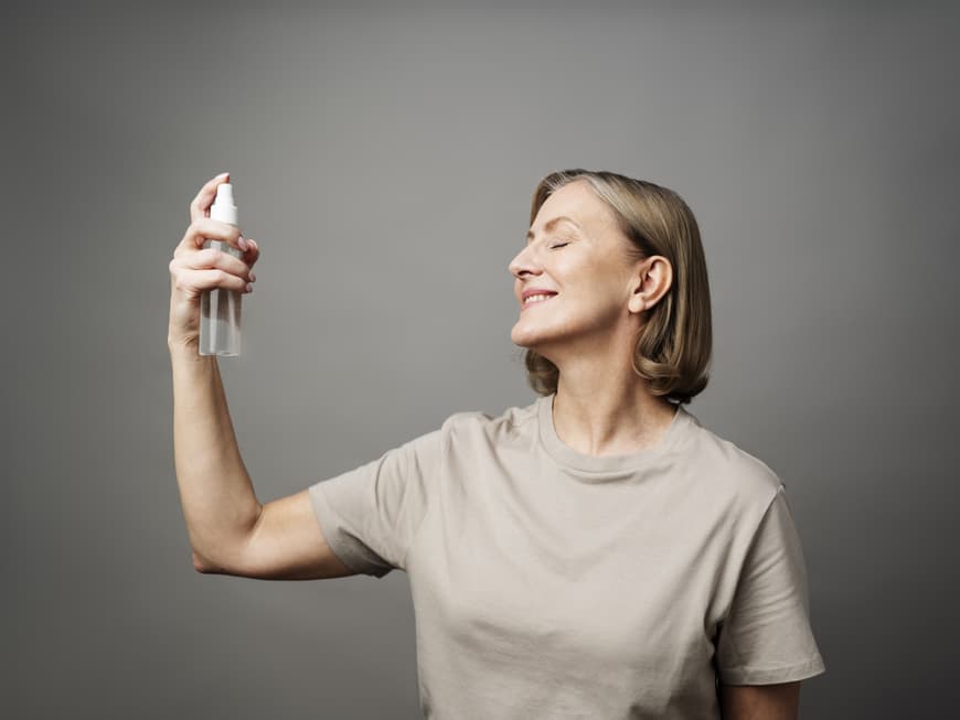 Frau sprüht Gesichtsspray in ihr Gesicht.