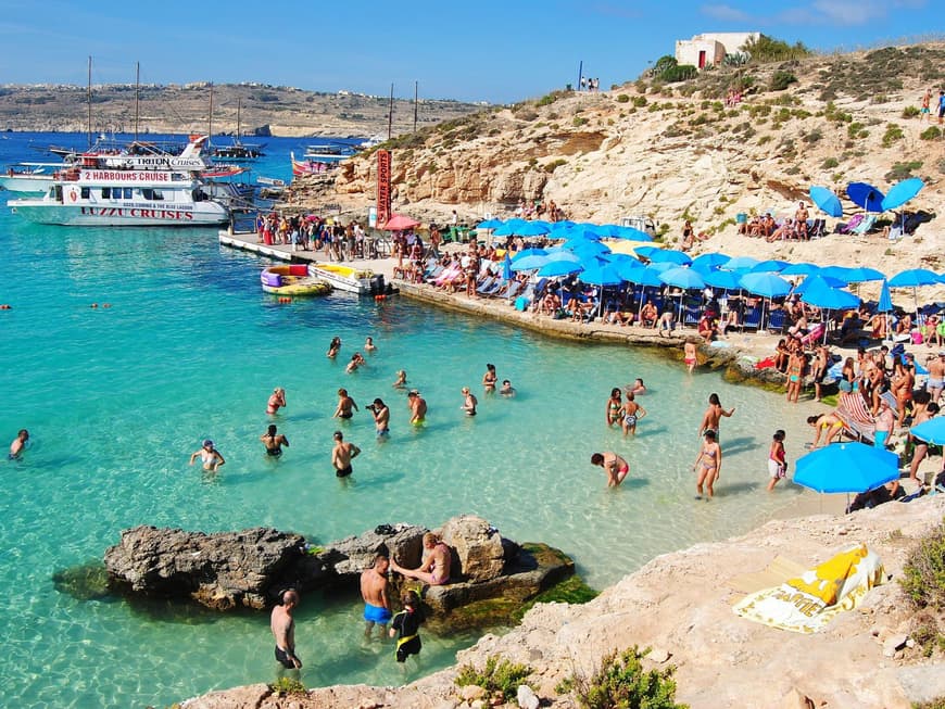Auf Comino wird es zur Hochsaison richtig voll. Viele Touristen am Strand im Wasser und unter Sonnenschirmen.