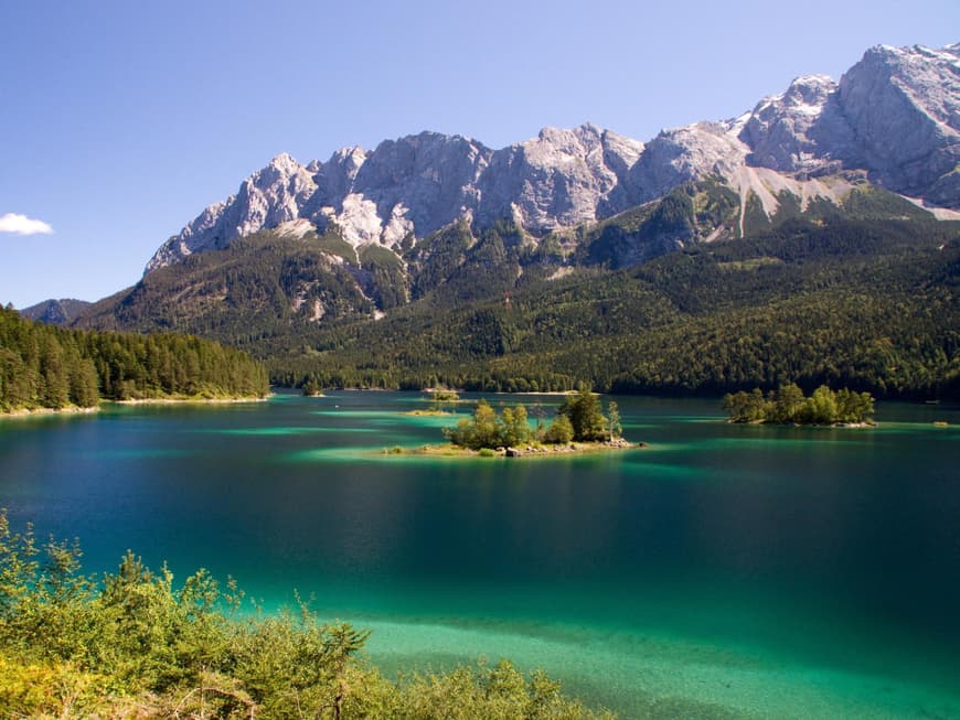Ein großer See mit Gebirge im Hintergrund und Wald drum herum.