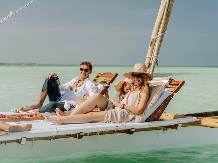 Mann und Frau mit Sonnenbrillen und sommerlicher Kleidung liegen auf einer Liege über dem Meer.