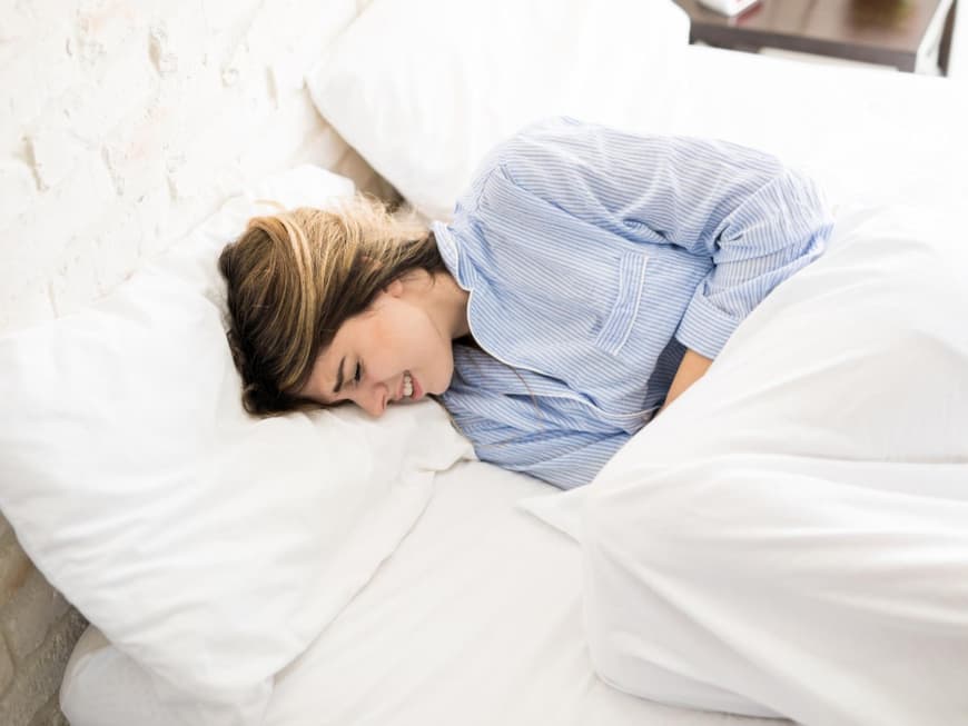 Eine Frau liegt mit Bauchschmerzen im Bett