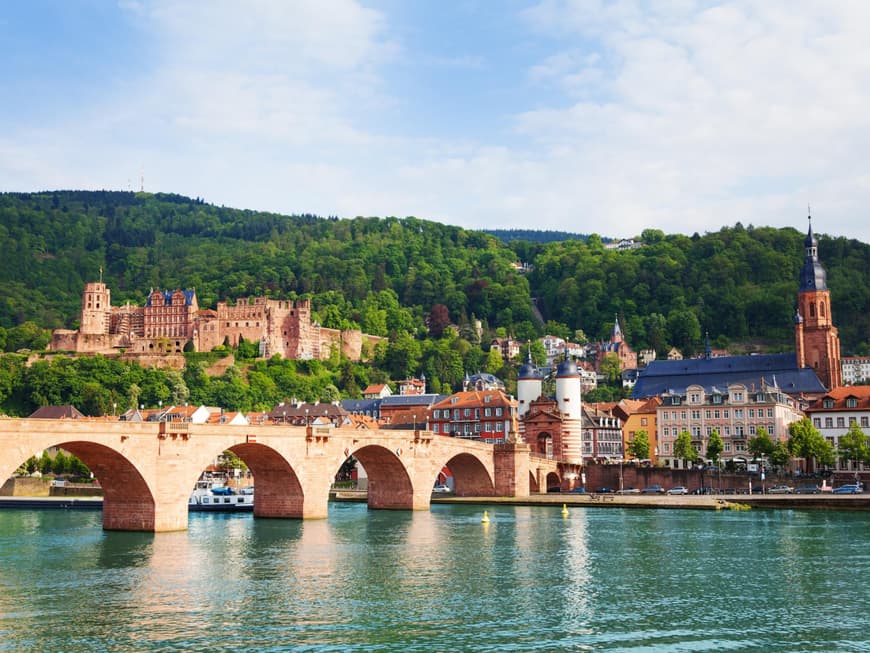 Eine Brücke im Wasser mit Häusern, Burgen und Wäldern im Hintergrund.