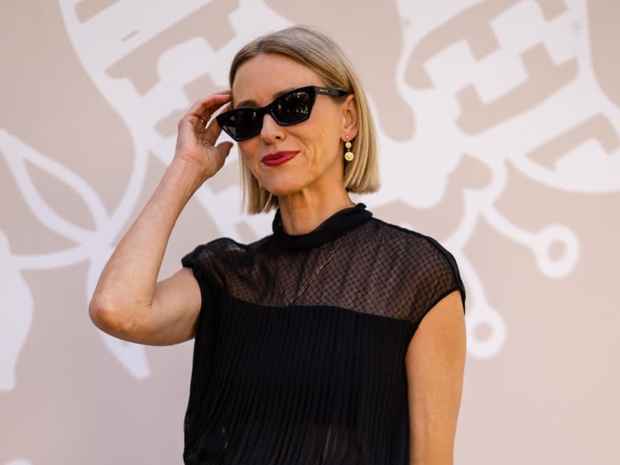 Frau mit kurzen, blonden Haaren, roten Lippen und einer schwarzen Sonnenbrille.