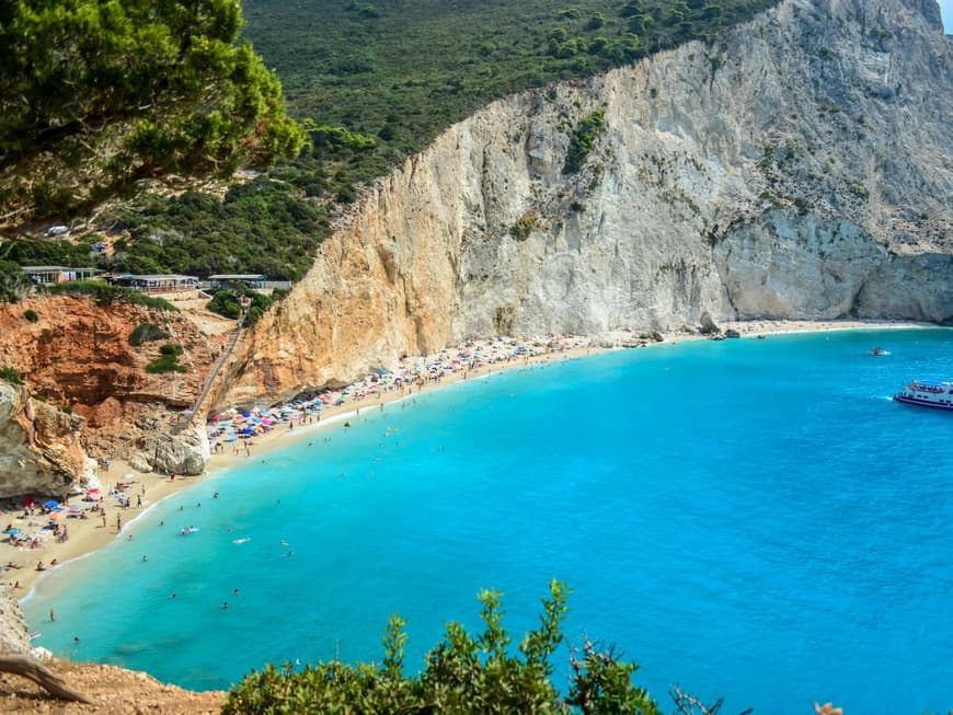 Lefkada ist ein atemberaubender Ort zum Urlaubmachen. Ein Blick auf einen schmalen Strand mit einem großen Hand dahinter. An dem Strand sind einige Menschen und Sonnenschirme.