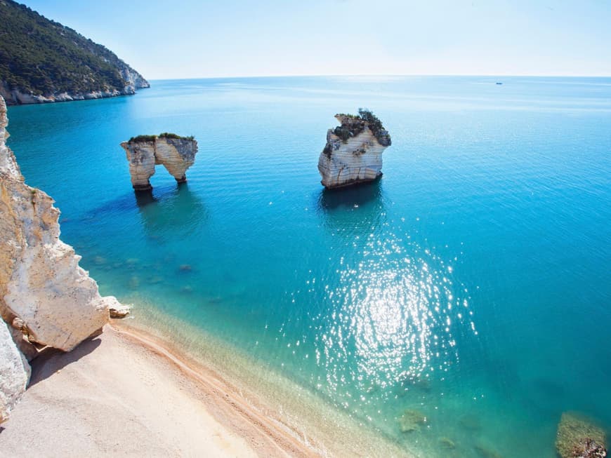 Türkisblaues Meer mit Felsen darin und einem Strand im Vordergrund.