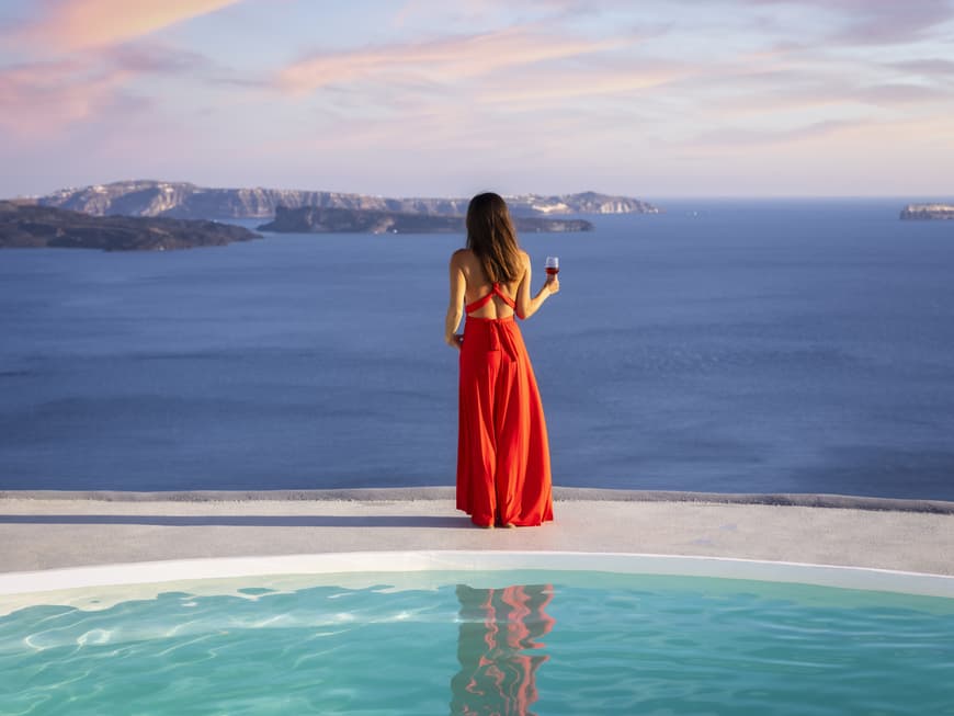 Frau steht in rotem Kleid am Pool und blickt aufs Meer.