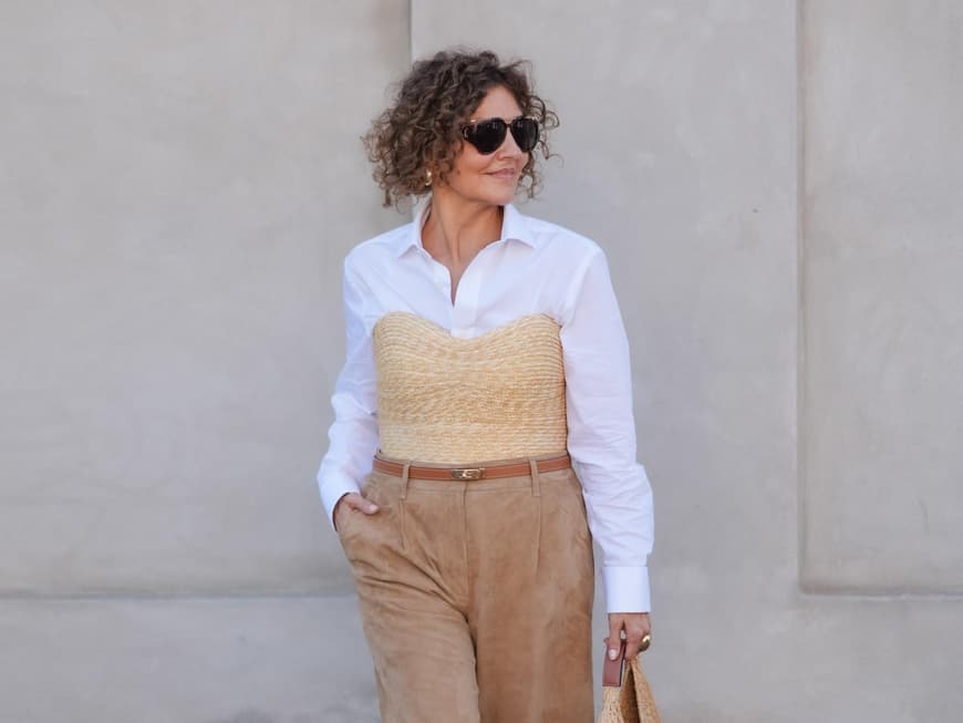 Ein Kurzhaarschnitt für lockiges Haar im Sommer ist praktisch und stylish zugleich. Frau mit lockigen Haaren trägt eine weiße Bluse mit einer Korb-Korsage und einer knielangen Hose.