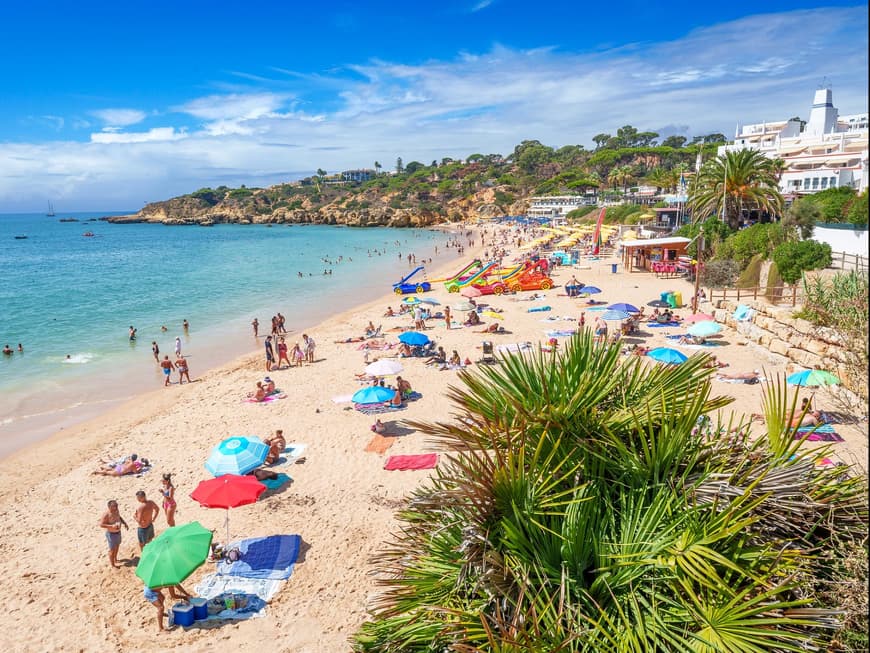 Der Praia da Oura ist besonders bei Familien beliebt. Strand mit vielen Urlaubern, Sonnenschirmen, Palmen und Tretbooten am Strand.