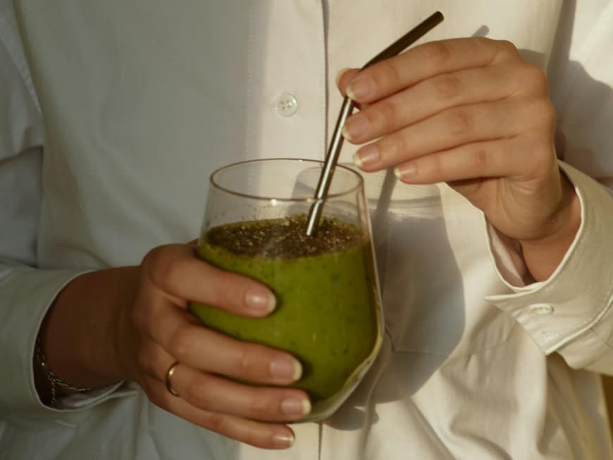 Frau hält ein Glas mit einem grünen Shake und einem Strohhalm in der Hand.
