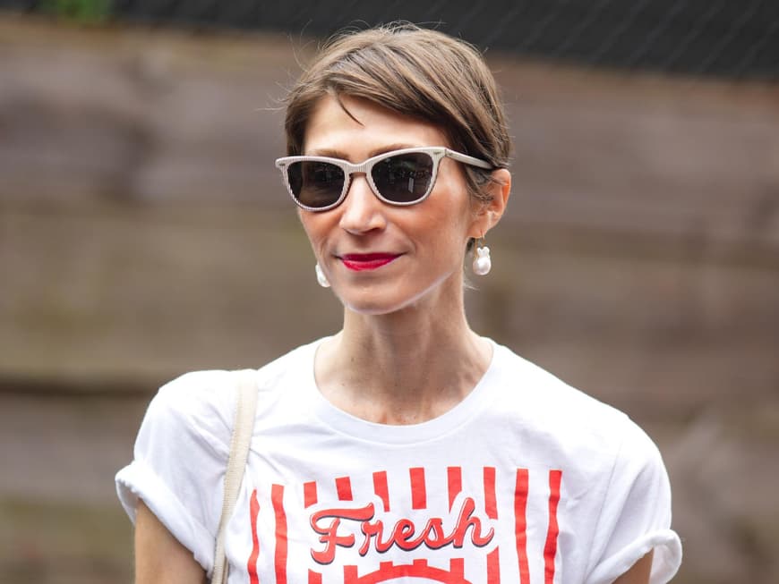 Frau mit braunhaarigem Kurzhaarschnitt, einer beigen Sonnenbrille und roten Lippen.