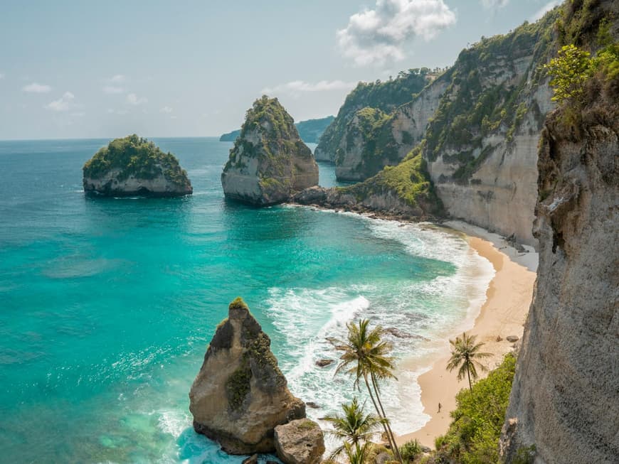 Ein Blick auf einen schmalen, leeren Strand umringt von Klippen und begrünten Felsen.