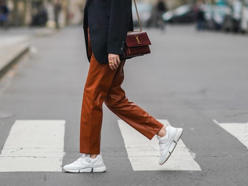 Frau mit Blazer trägt eine rötliche Hose und weiße Sneaker.