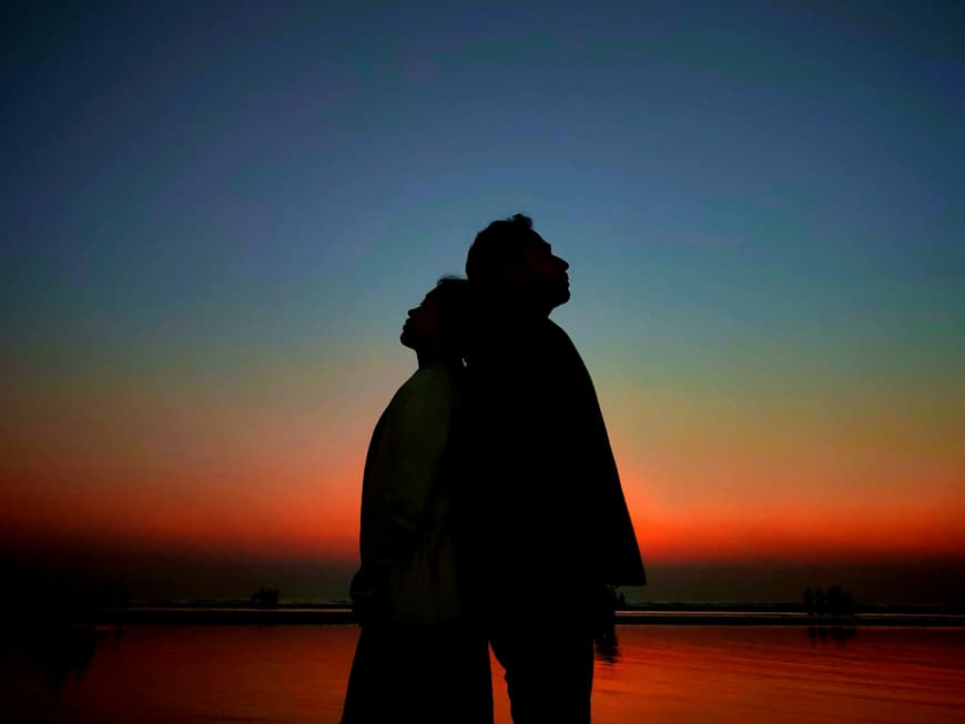 Ein Paar steht Rücken an Rücken vor dem Nachthimmel.