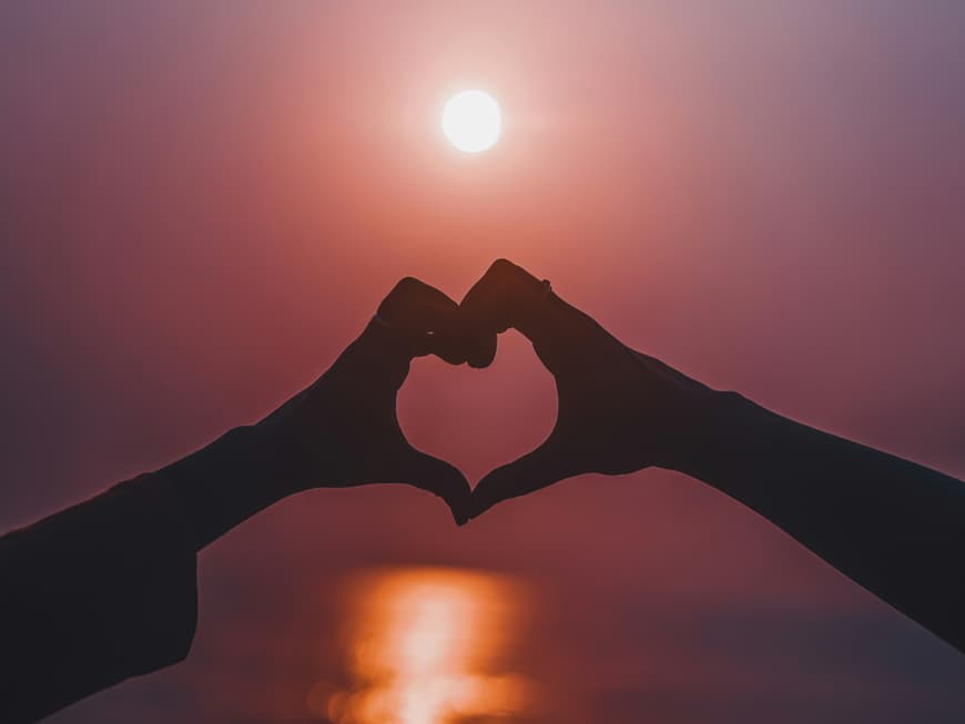 Hände formen ein Herz vor dem Abendhimmel