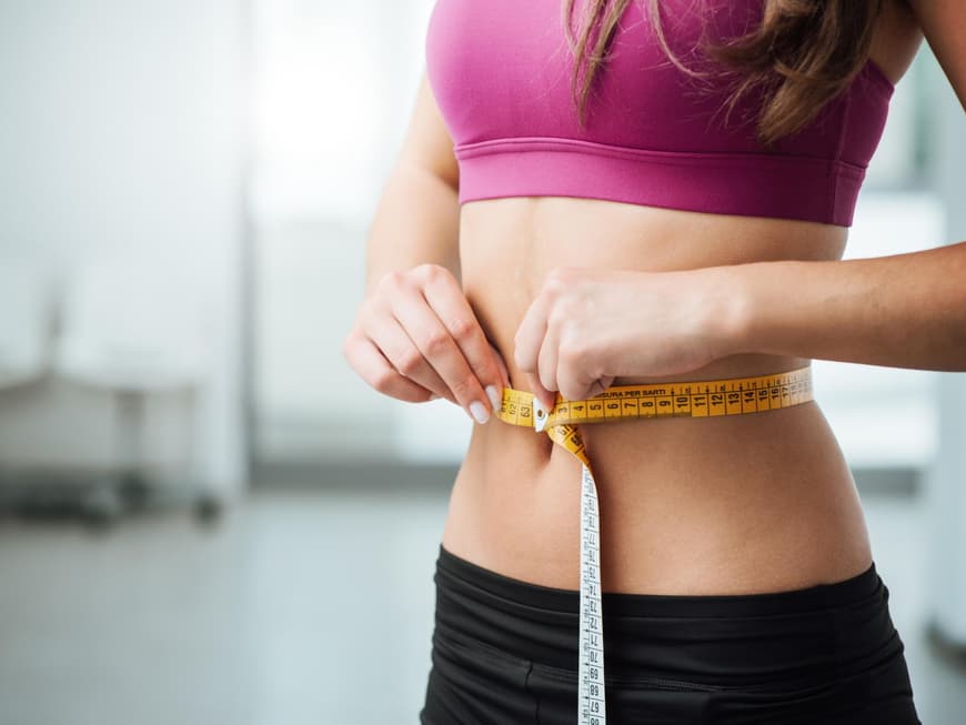 Eine Frau hält ein Maßband um ihre Taille