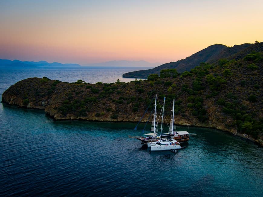 Eine Bucht bei Sonnenaufgang mit einer Gulet und einer Yacht im Wasser.