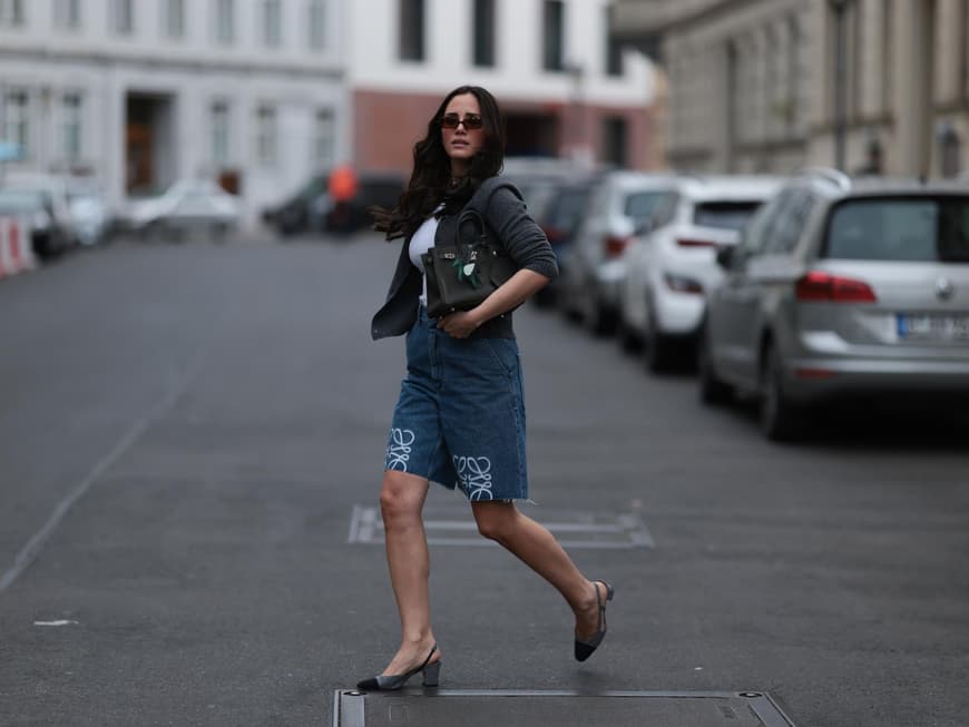 Frau mit dunklen Haaren und Sonnenbrille trägt Jeans-Shorts mit Slingback-Pumps.