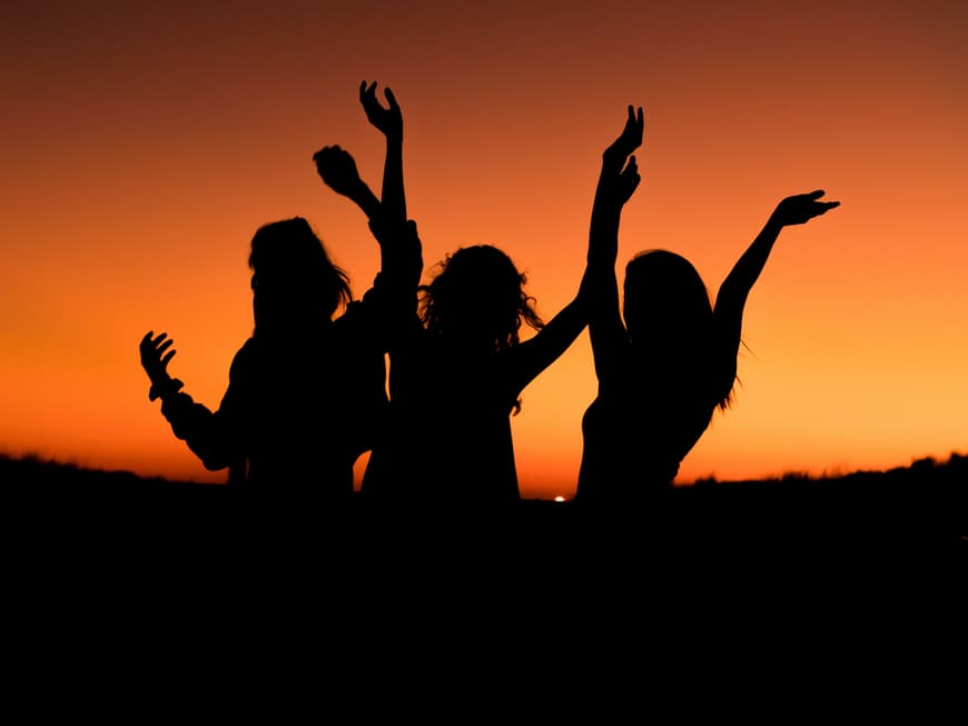 Drei Sternzeichen lassen sich nicht unterkriegen, sondern blühen nach einer Trennung erst richtig auf. Drei Frauen tanzen ausgelassen vor dem Sonnenuntergang.
