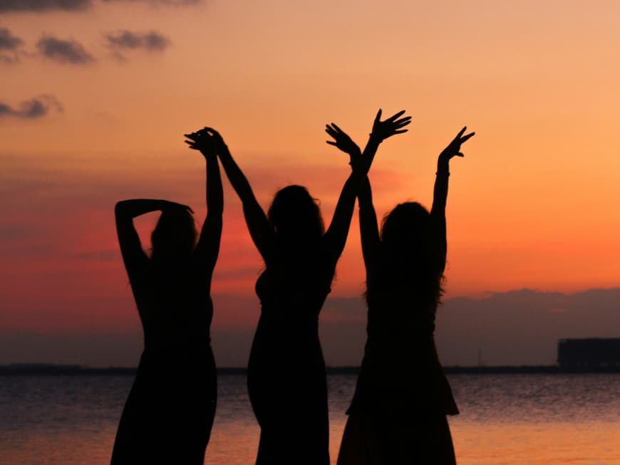 Drei Frauen tanzen vor dem Abendhimmel