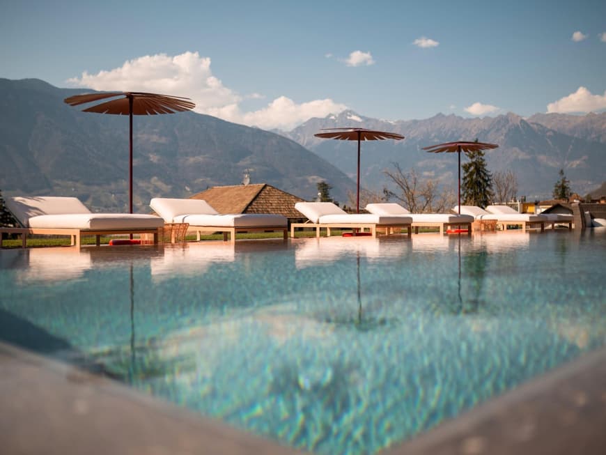 Ein Infinity Pool ist ein echtes Highlight in einem Hotel. Infinity Pool mit Liegen und Sonnenschirmen und Bergen im Hintergrund.