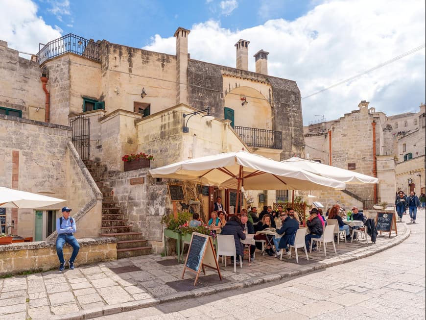 Entspannt in Cafés sitzen kannst du hier perfekt. Ein Cafe vor einer Mauer und Burg mit Touristen am Essen.