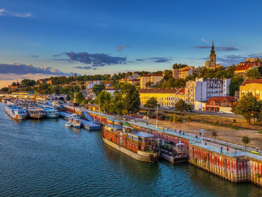 Ein Blick über den Hafen von Belgrad mit Schiffen im Wasser und Häusern an Land, die von der Sonne beleuchtet werden.