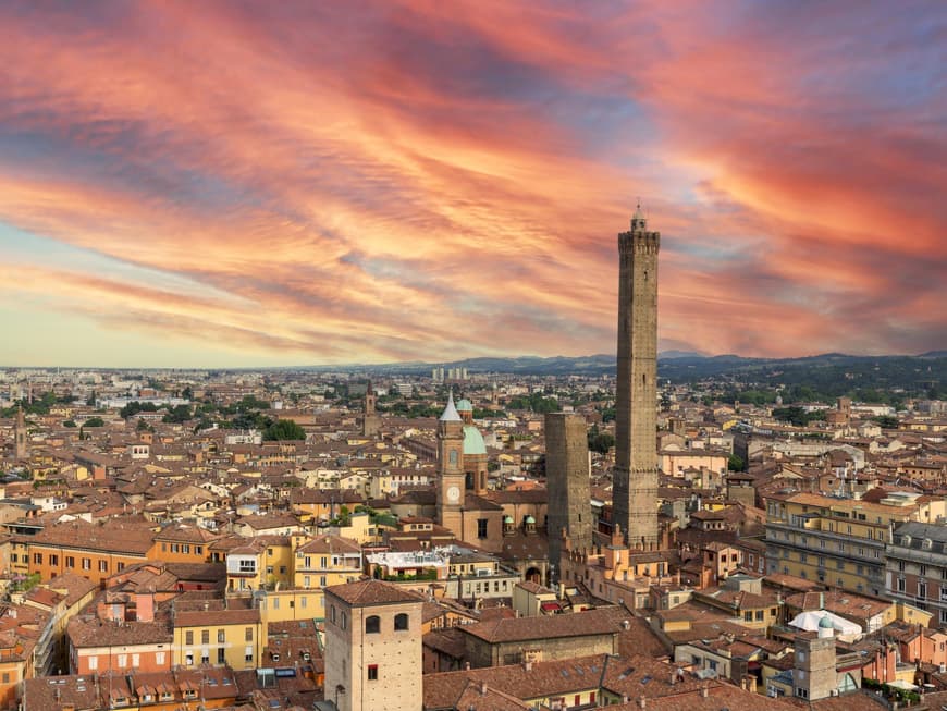 Bologna ist eine Stadt in Italien, die mit Gastronomie, Historie und Charme überzeugt. Ein Blick über die Dächer von Bologna bei einem rötlichen Himmel.