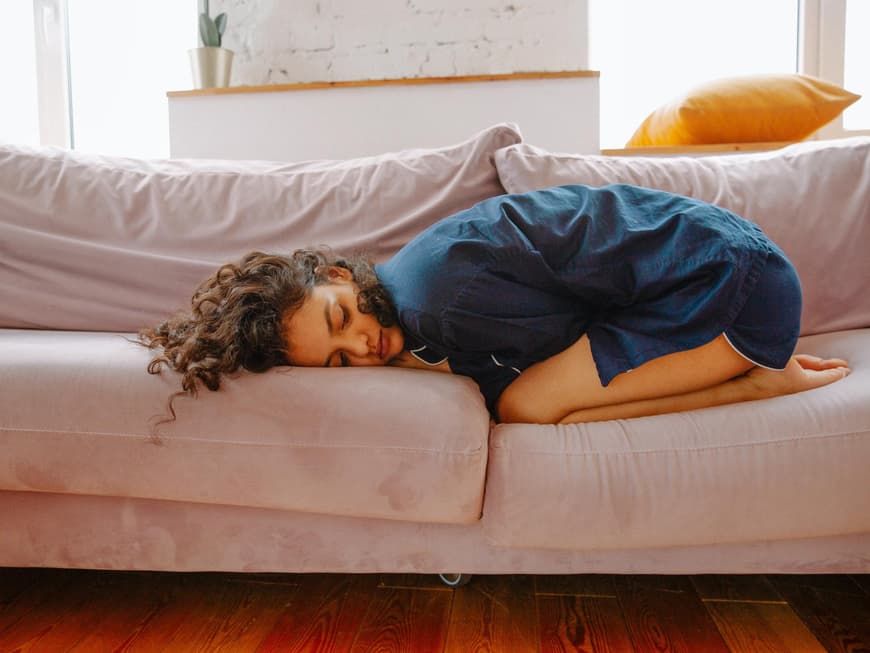 Frau liegt mit Periodenschmerzen auf der Couch
