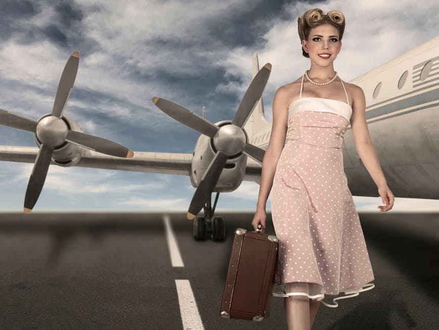 Frau im Sixties-Look mit Koffer vor einem Flugzeug