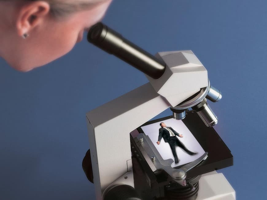 Frau untersucht Mann unterm Mikroskop