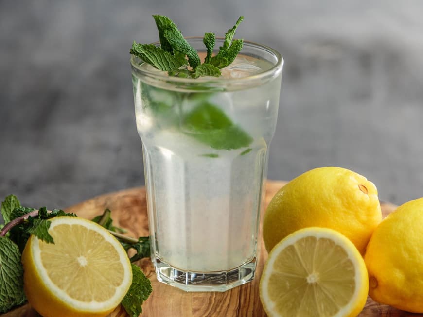 Ein großes Glas mit Wasser und frischer Minze drin, drum herum liegen aufgeschnittene Zitronen.